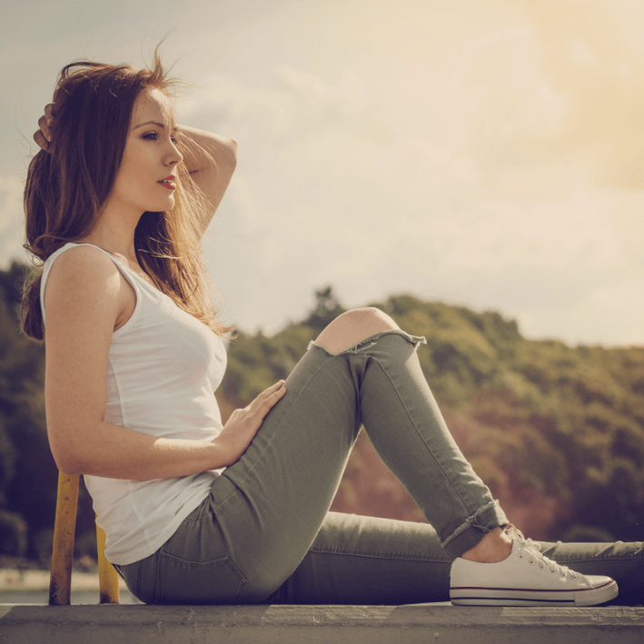 Vrouw zittend in de natuur, genietend van de zon met casual kleding en een ontspannen uitstraling.