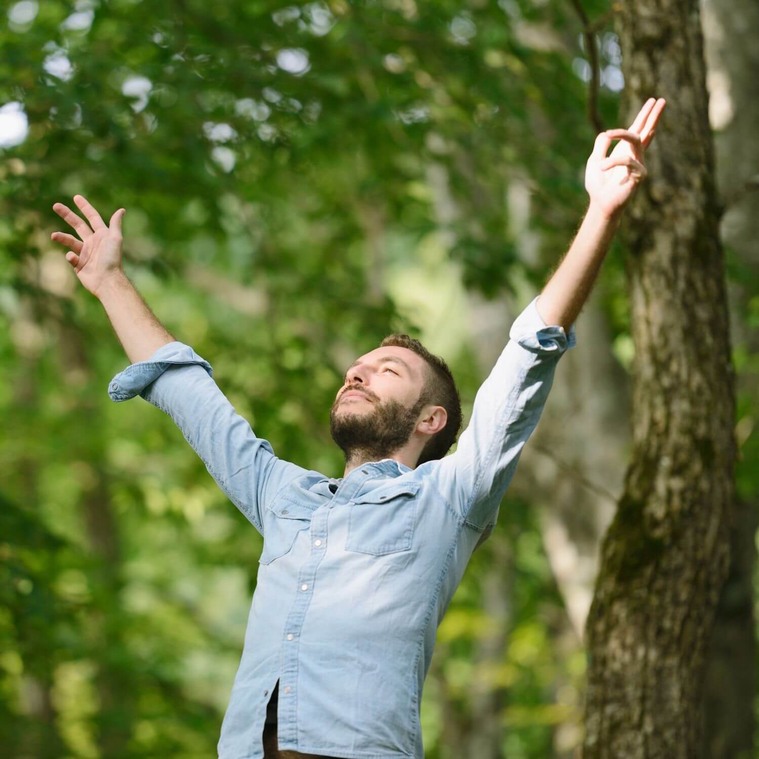 Vrolijke man die zijn armen omhoog steekt in een groene omgeving, genietend van de natuur.