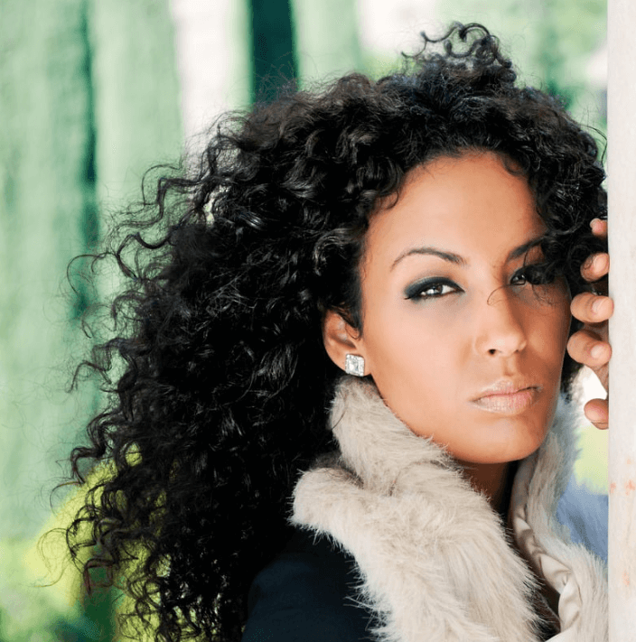 Een vrouw met krullend haar, met een stijlvolle uitstraling en een elegante look, poseert buiten.