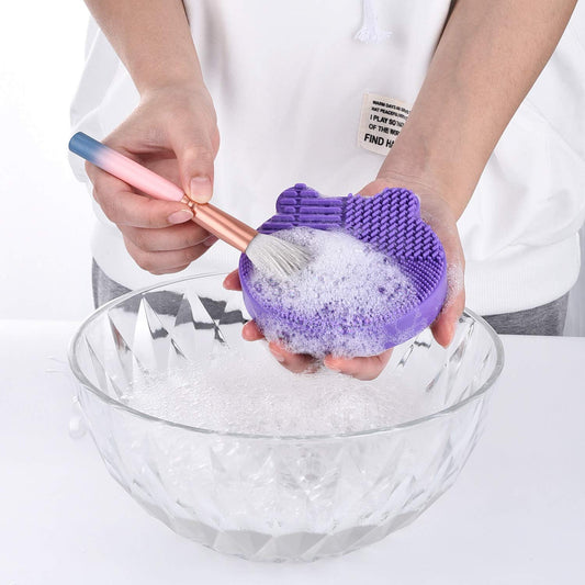 Jovyx CleanMat – Siliconen Make-upborstelreiniger in gebruik met borstel en zeep in een kom.