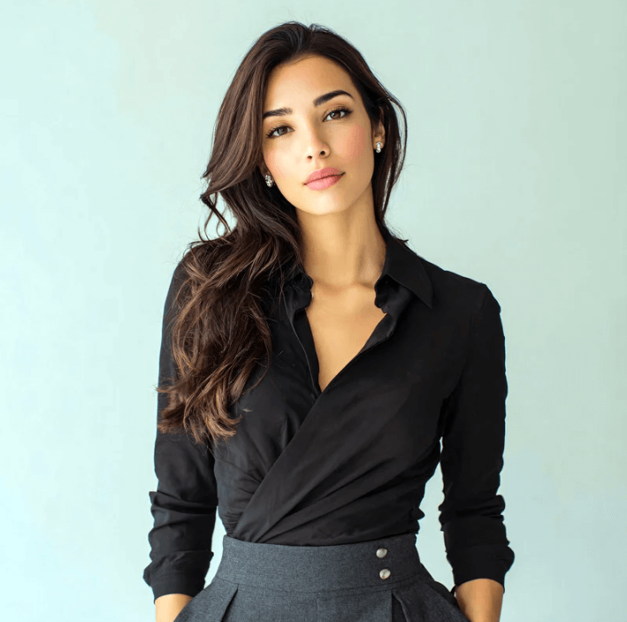 Model met stralend haar in zwarte blouse en grijze rok, poseert tegen een lichte achtergrond.