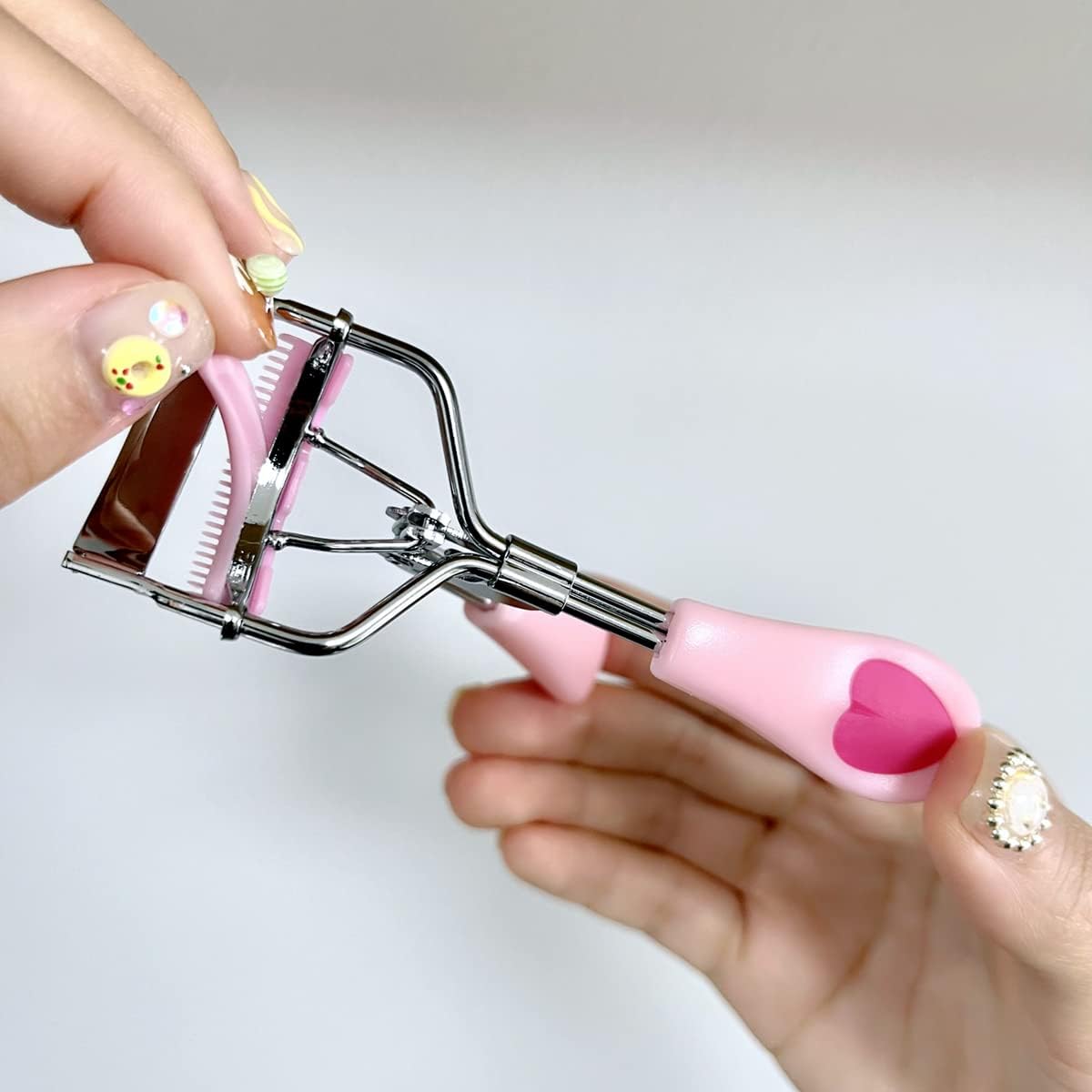 Jovyx LashPro – Roestvrijstalen Wimperkruller in handen met roze handvatten en roestvrijstalen frame.